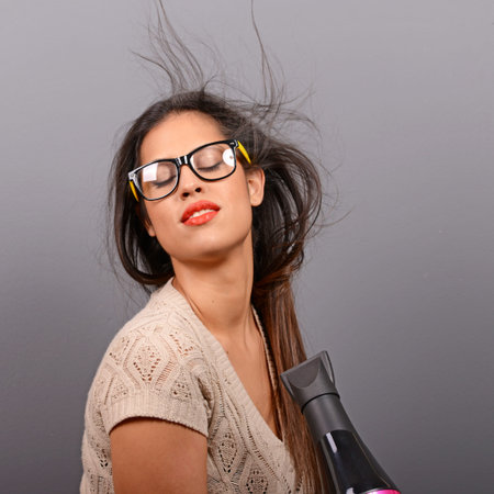 Portrait of a woman holding hair dryer against gray background