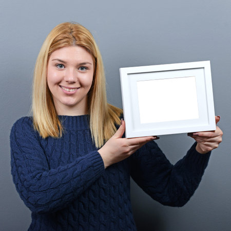 Portrait of smiling woman holding blank photo frame against gray background