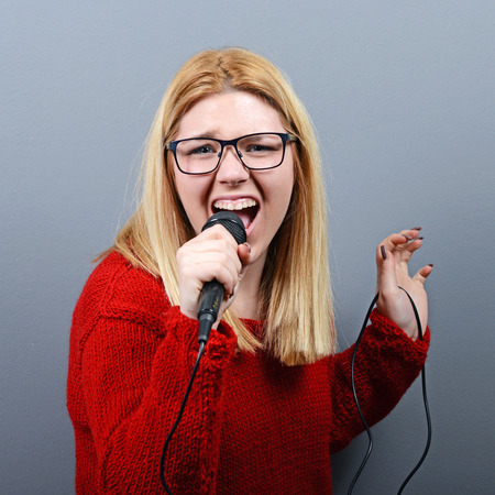 Beautiful woman singing with the microphone against gray backgroundの写真素材