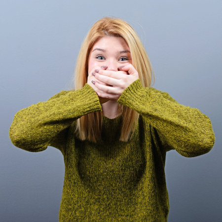 Woman covering her mouth with hands against  gray background