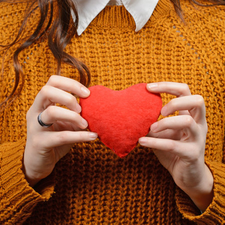 Beautiful happy woman holding heart in hands against gray background