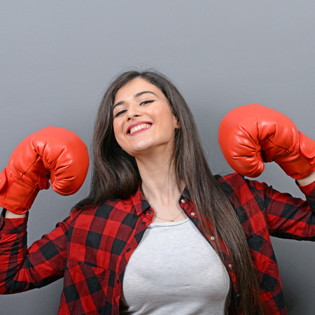 Portrait of young woman posing with boxing gloves against gray backgroundの写真素材