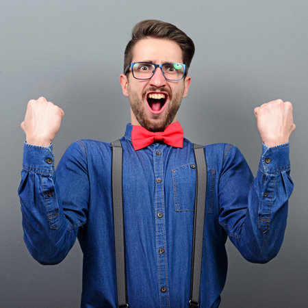 Portrait of ecstatic young man celebrating victory or win against gray background