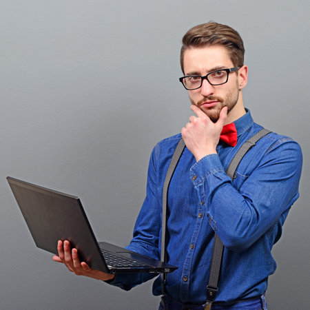 Handsome young businessman holding laptop against gray background