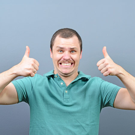 Portrait of a man showing thumb up or ok sign against gray backgroundの写真素材