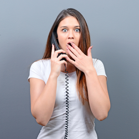 Portrait of woman having unpleasant phone calll against gray backgroundの写真素材