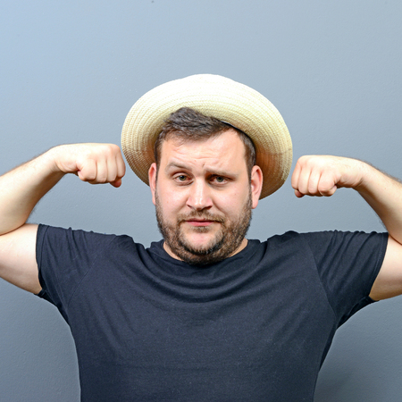 Portrait of funny chubby man wearing straw hat showing musclesの写真素材
