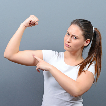 Pretty young brunette woman showing bicep on her arm against gray backgroundの写真素材