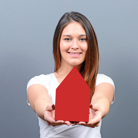 Young woman holding house against gray background -  Real estate conceptの写真素材