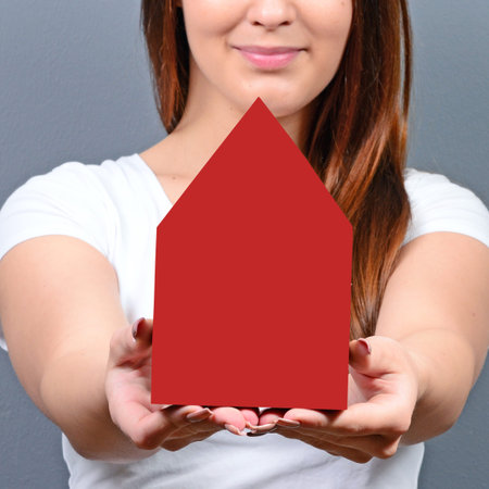 Young woman holding house against gray background -  Real estate conceptの写真素材