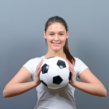 Portrait of girl holding football against gray backgroundの写真素材