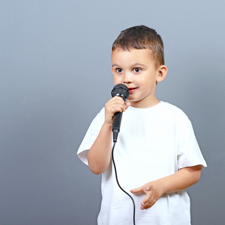Cute little boy kid singing on microphone against gray backgroundの写真素材