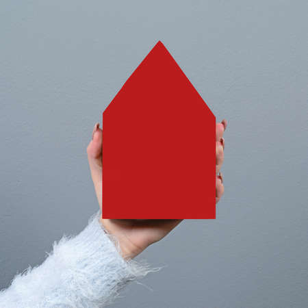 Young woman holding house against gray background -  Real estate conceptの写真素材