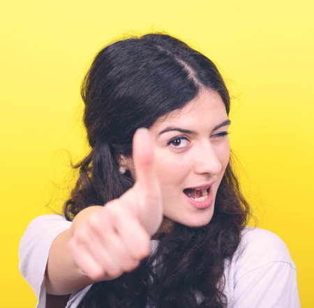 Portrait of happy woman with thumbs up against yellow background