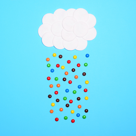 Multicolored sweets falling from cotton clouds against blue background - Flat layの写真素材