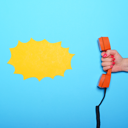 Empty comic book yellow cloud next to retro orange phone tube held by woman hand - Flat layの写真素材