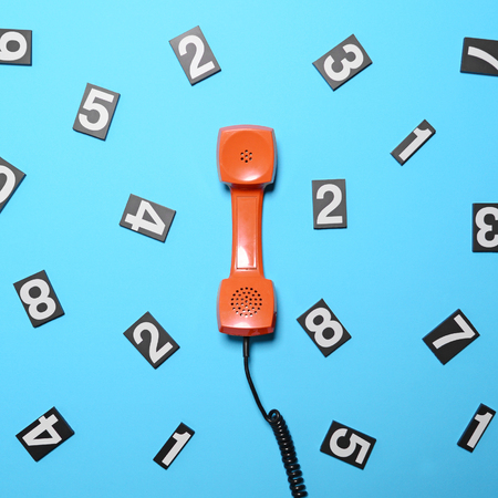 Retro orange telephone tube with numbers around it on blue background - Flat layの写真素材