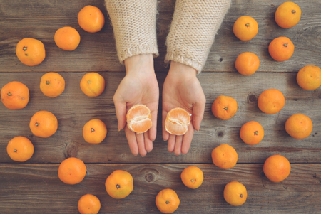 Flat lay view of woman hands peeling fresh mandarines on wooden table - Autumn conceptの写真素材