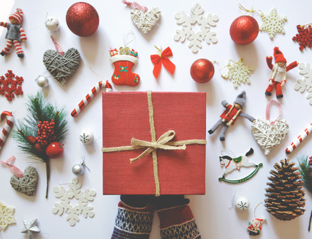 Flat lay of Christmas decoration and ornaments on white backgroundand woman hand holding red gift box - Trendy minimal flat lay designの写真素材