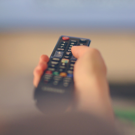 Hand holding remote tv controller towards televisonの写真素材