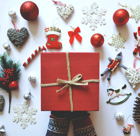 Flat lay of Christmas decoration and ornaments on white backgroundand woman hand holding red gift...