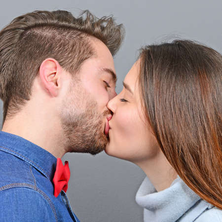 Young couple sharing romance and kissing against gray backgroundの写真素材