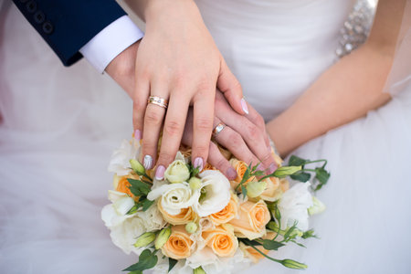 Hands and rings of the bride and groom on wedding bouquet