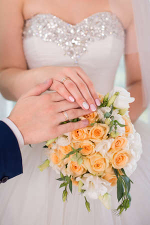 Hands and rings of the bride and groom on wedding bouquetの写真素材