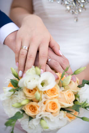 Hands and rings of the bride and groom on wedding bouquetの写真素材