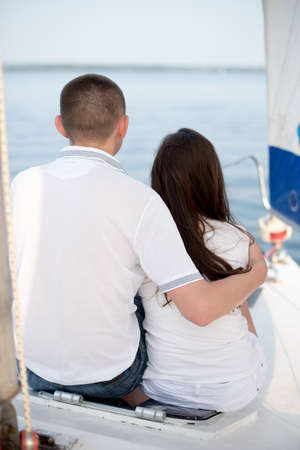 Back view of beautiful young loving couple sitting and hugging on yacht with sailの写真素材