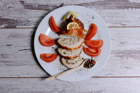 Baked chicken rolls with tomato and lemon and spices on a white plate on a white wooden tableの写真素材