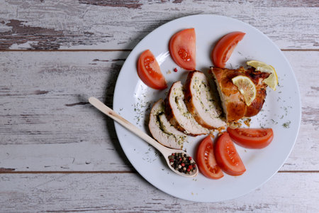 Baked chicken rolls with tomato and lemon and spices on a white plate on a white wooden table