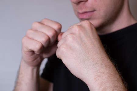 Close-up portrait of a young man standing in boxer position and ready to fight clenching his fists, in black t-shirtの写真素材