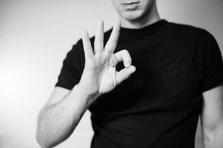 Serious young man showing ok gesture isolated on gray wall background in black t-shirtの写真素材