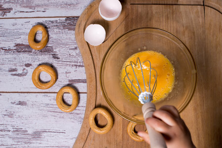 Egg yolk and white in glass bowl and wire whisk over dark weathered wooden table, cutting Boardの写真素材