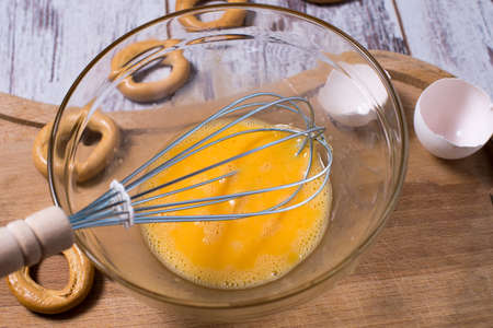 Egg yolk and white in glass bowl and wire whisk over dark weathered wooden table, cutting Boardの写真素材
