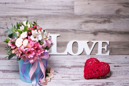 beautiful floral arrangement in a hat box with the inscription LOVE and action figure heart , shabby white wooden tableの写真素材