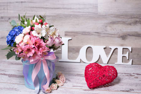 beautiful floral arrangement in a hat box with the inscription LOVE and action figure heart , shabby white wooden tableの写真素材