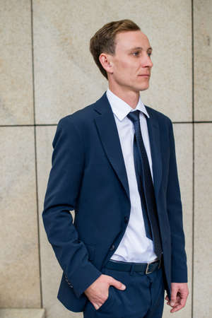 Young and successful. Handsome young businessman looking away while walking outdoors with office building in backgroundの写真素材