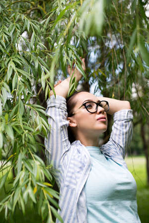 Portrait of young beautiful woman in glasses, on a green background summer nature.の写真素材