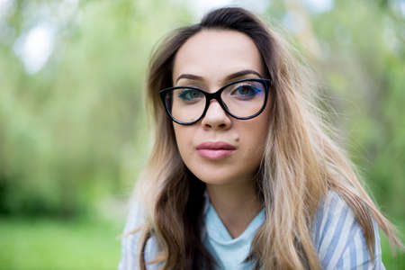 Portrait of young beautiful woman in glasses, on a green background summer nature.の写真素材