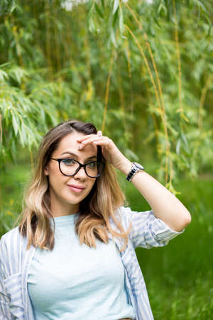 Portrait of young beautiful woman in glasses, on a green background summer nature.の写真素材