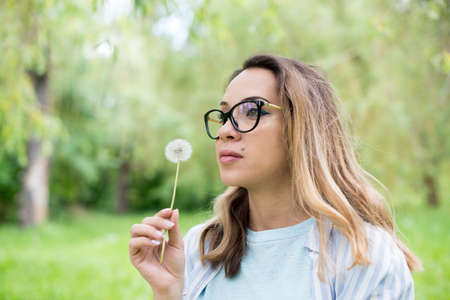 Portrait of a beautiful young woman blowing dandelion flowerの写真素材