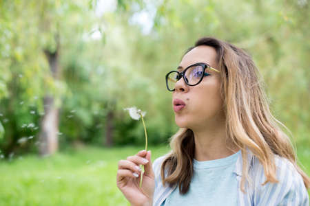 Portrait of a beautiful young woman blowing dandelion flowerの写真素材
