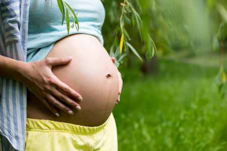 Beautiful belly of young pregnant woman against green spring background.の写真素材