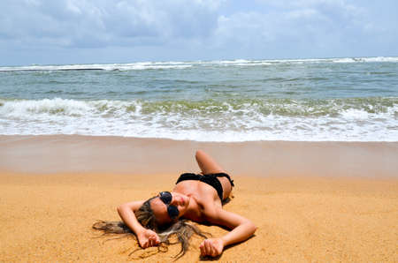 A beautiful girl in glasses lies on the shore of the oceanの写真素材