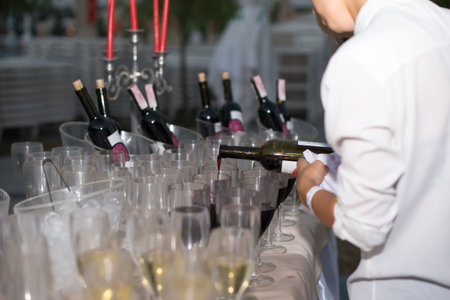 Waiter bartender pouring Red wine into glasses at party event.