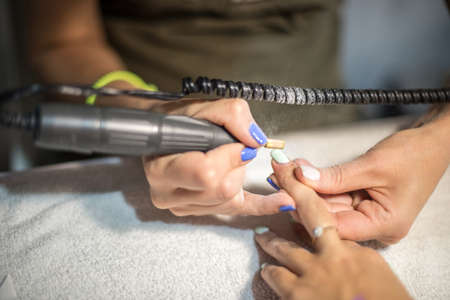 Hardware manicure. Removal of old gel varnish in the salon. Manicure master doing beauty procedure for client, closeup and top view.の写真素材