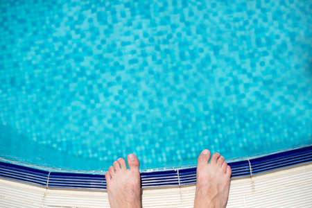 Pair of feet standing on stone border in front of swimming pool.の写真素材