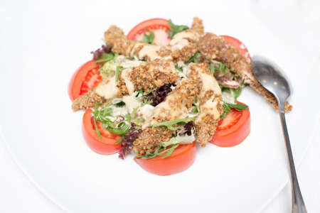fried in a breaded chicken and fresh vegetable salad close-up on a plate on a white table. view from aboveの写真素材